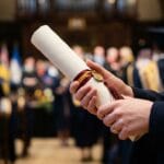 Dłonie studenta trzymające dyplom magisterski na uroczystości obrony
